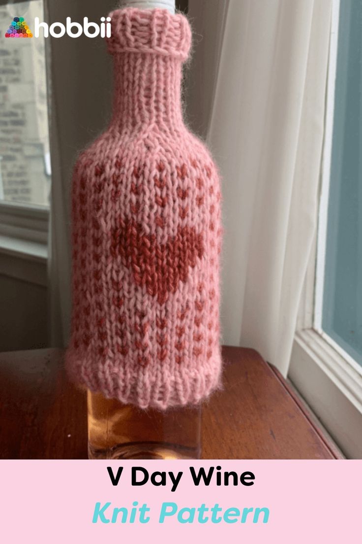 a knitted wine bottle sitting on top of a wooden table next to a window