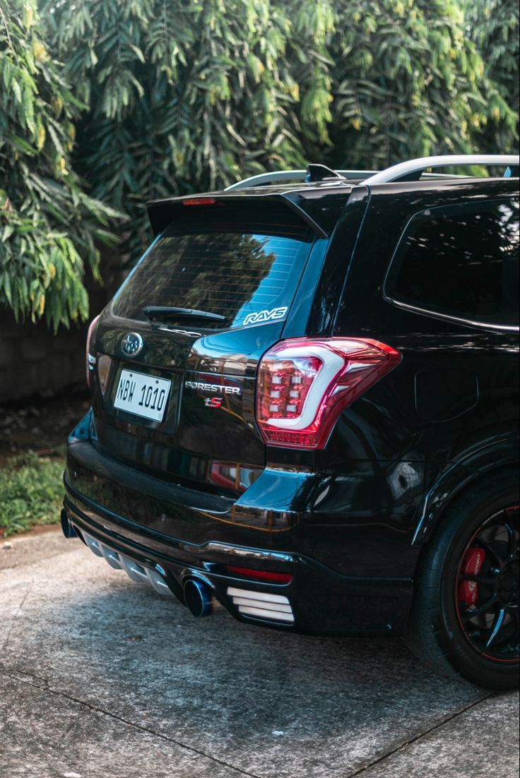 the back end of a black suv parked in front of some bushes