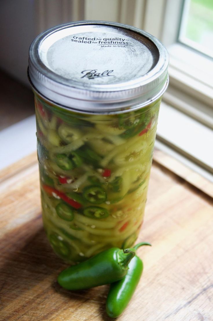 a jar filled with green peppers sitting on top of a wooden table