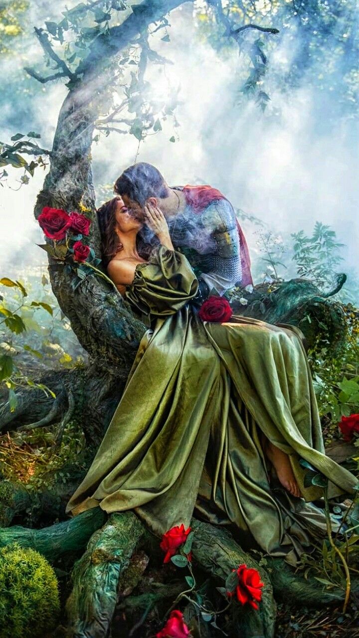 a man and woman are kissing on a tree in the woods with flowers around them