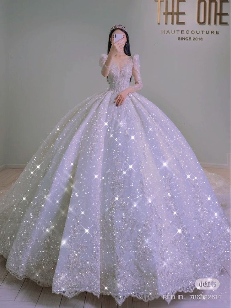 a white ball gown with stars on the skirt and long sleeves is displayed in front of a wall