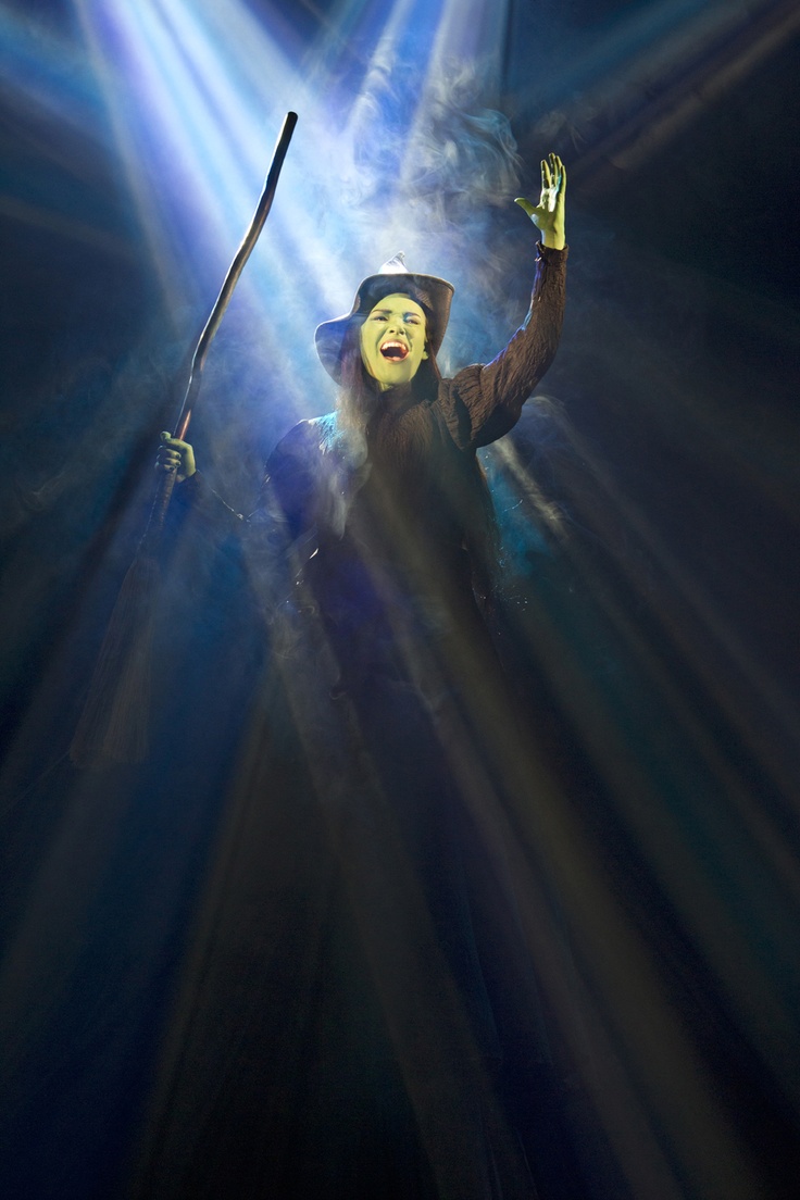 a woman dressed in costume holding a wand and wearing a hat with her hands up