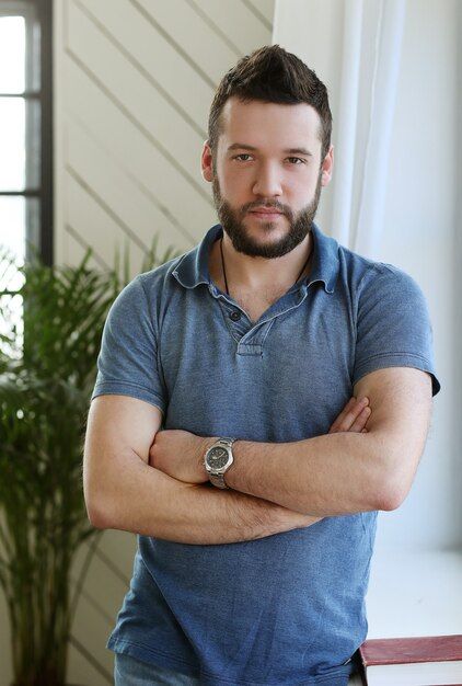 a man with his arms crossed standing in front of a window and looking at the camera