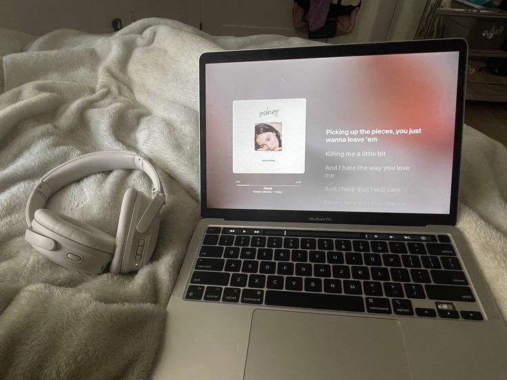 an open laptop computer sitting on top of a bed next to headphones and a remote control