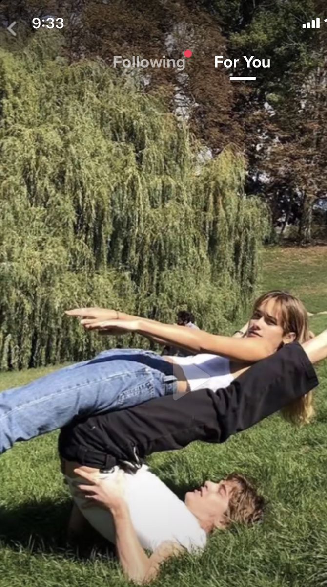 a man and woman laying on the grass in front of some trees with their arms around each other