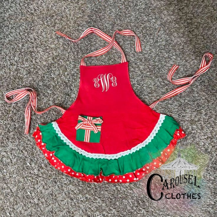 a red apron with green and white ruffles on the bottom has a monogrammed bow