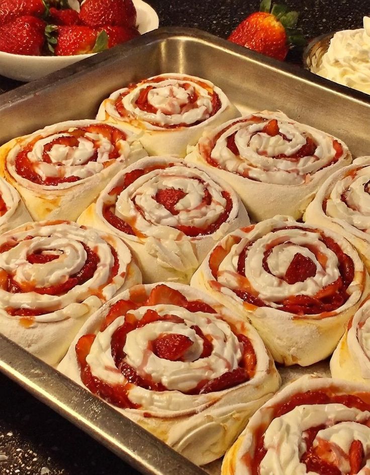 a pan filled with rolls covered in icing next to strawberries