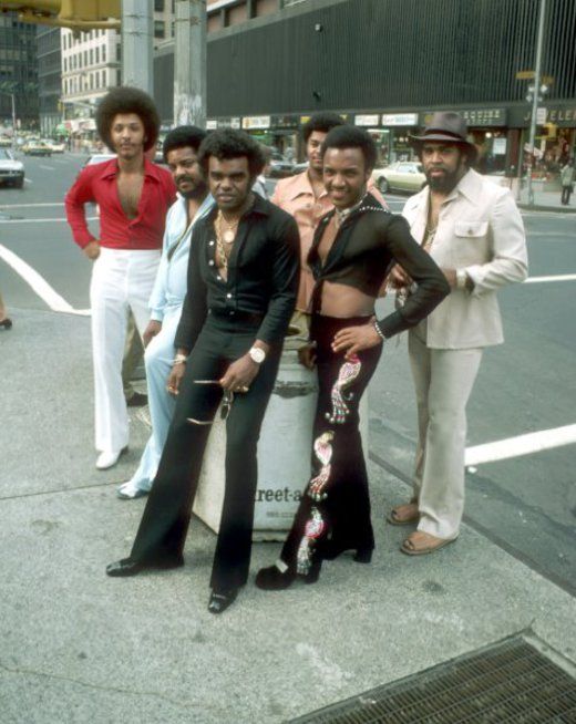 a group of men standing next to each other on a city street with buildings in the background