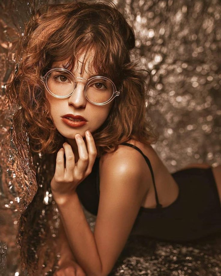 a woman wearing glasses leaning against a wall