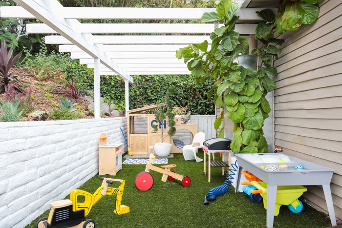 an outdoor play area with toys on the grass and plants growing in the back yard