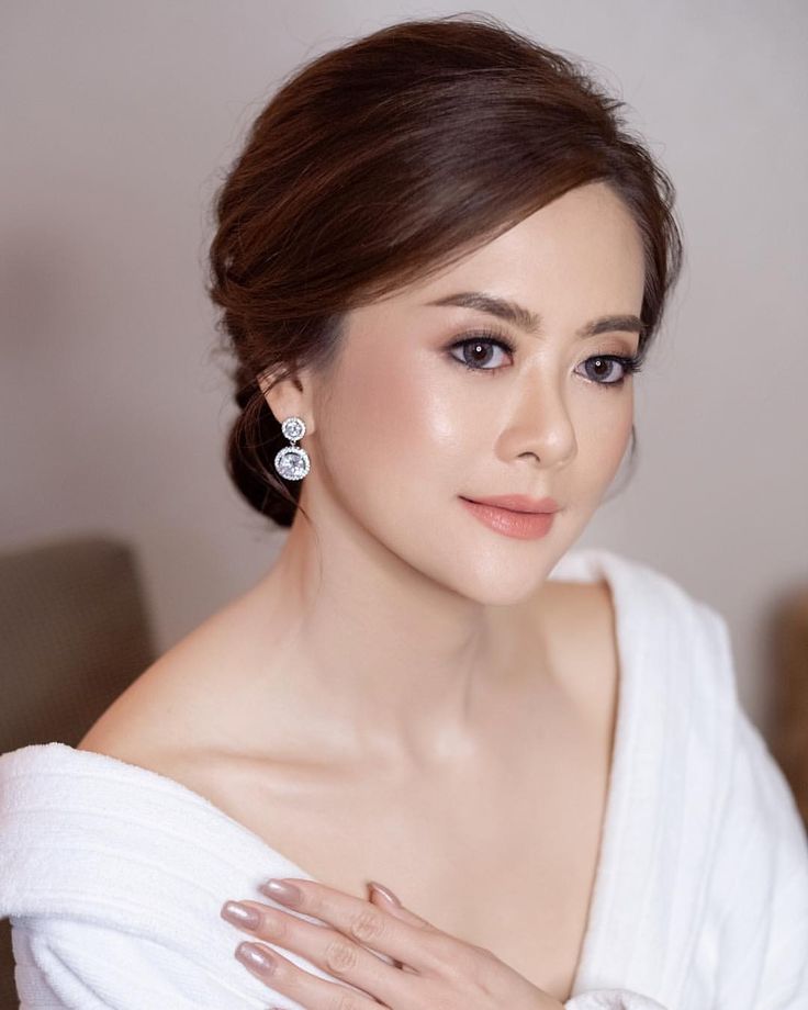 a woman in a white dress with her hands on her chest, wearing earrings and posing for the camera