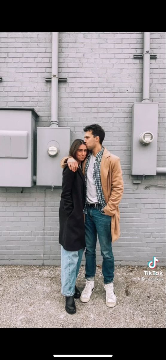 a man and woman standing next to each other in front of a wall with urinals