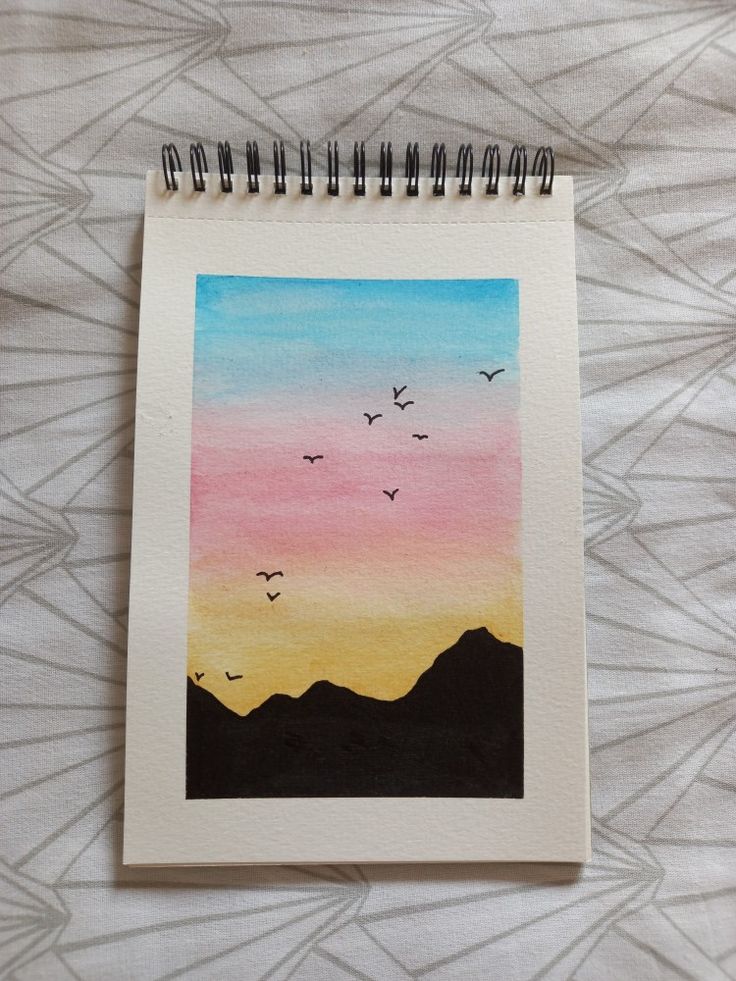 a spiral notebook with watercolors on it and birds flying in the sky at sunset