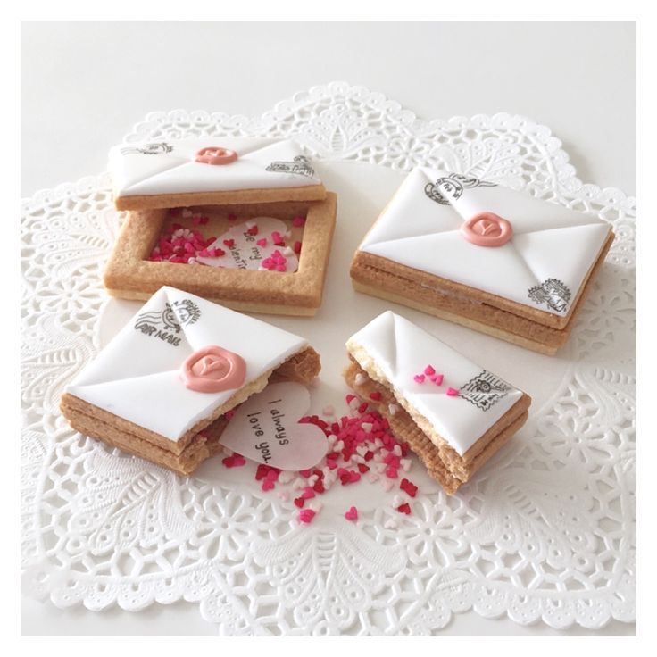 four decorated cookies sitting on top of a white doily with pink sprinkles