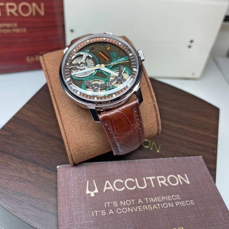 Recreating the stunning visual impact of the original open dial design with the exact-same signature green accents, the Accutron x La Palina Spaceview 2020 boasts a brown open-work dial with signature Accutron green accents and brown outer ring, light green super luminous markers, hour and minute hands and warm yellow second hand. Finished on a matching genuine brown alligator strap, the watch comes with a humidor set with cigar cutter and ten cigars. The custom-designed humidor is 100% handmade Modern Brown Watch With Skeleton Dial, Brown Skeleton Dial Watch For Formal Occasions, Timeless Brown Watch With Skeleton Dial, Luxury Green Watch With Analog Display, Brown Chronometer Watch With Round Dial, Brown Watch With Chronometer And Round Dial, Luxury Green Watch For Business, Green Watches With Skeleton Dial, Green Skeleton Dial Watch