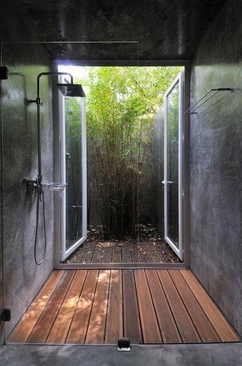 an open shower stall with wooden flooring and bamboo trees in the backround