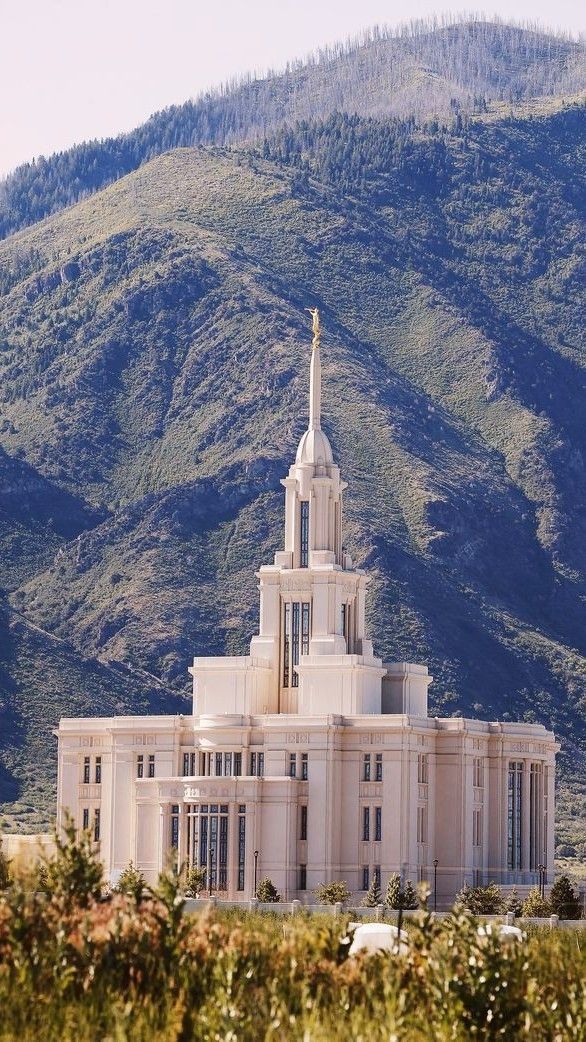 a large white building with a steeple in front of a mountain and hills behind it