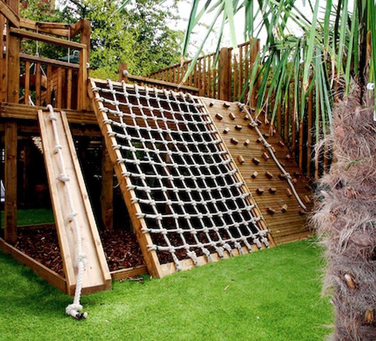 a wooden slide set in the grass next to a palm tree and a large potted plant