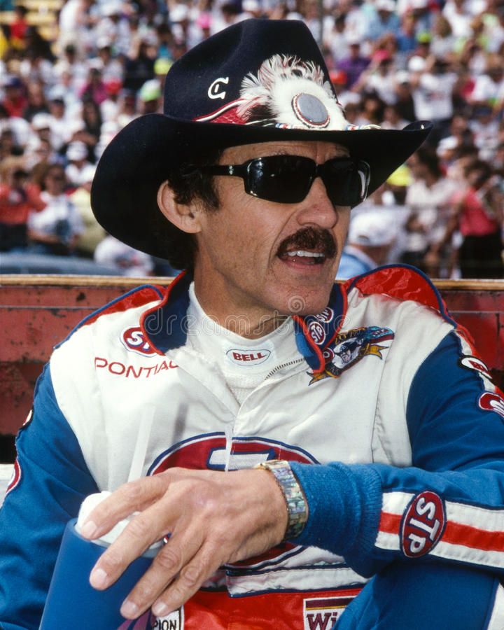 a man in a cowboy hat and sunglasses sitting on a bench at a sporting event