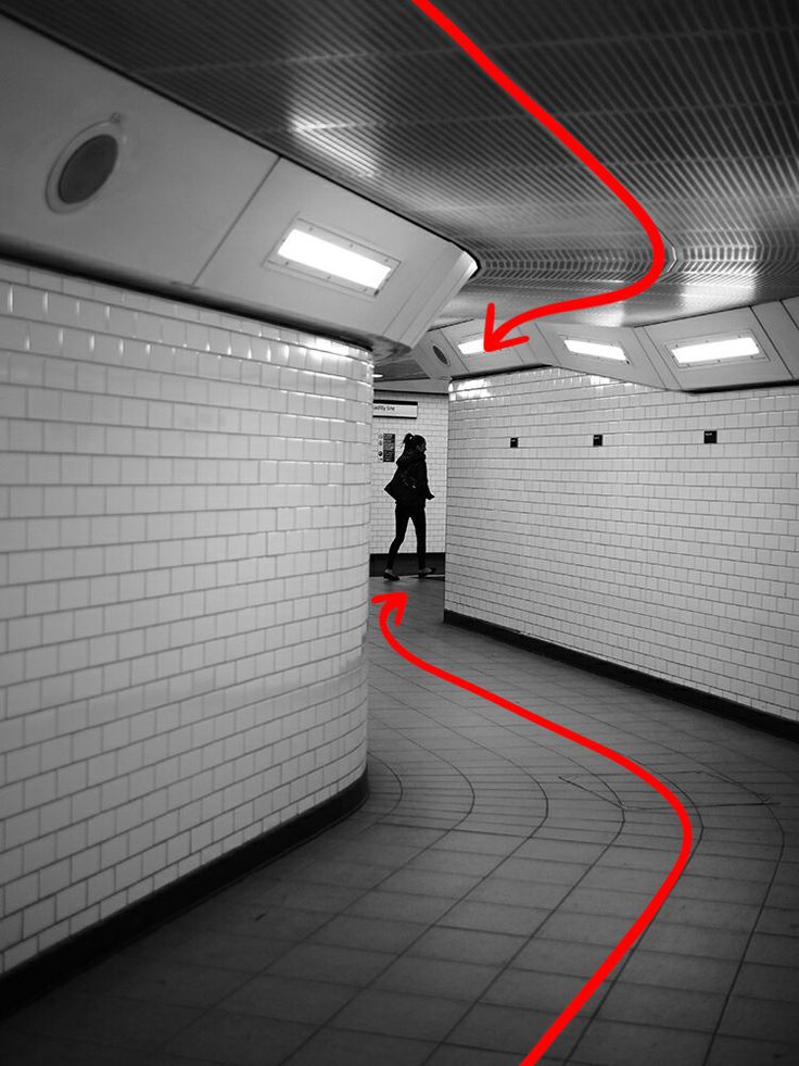 a person walking through a subway tunnel with red lines on the floor and white walls