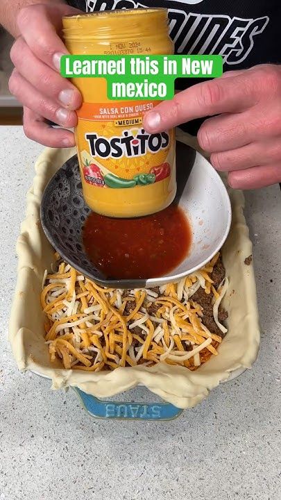 someone is pouring sauce into a bowl with shredded cheese on the bottom and other ingredients in it