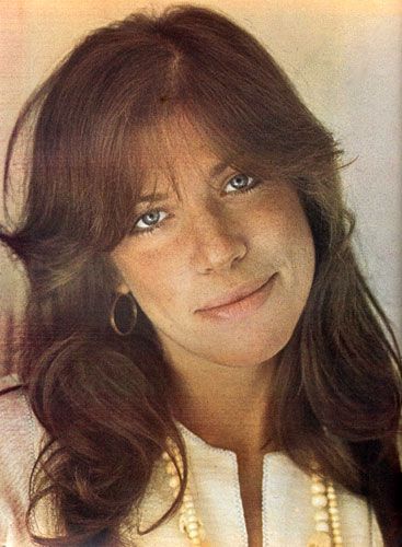 an old photo of a woman with long hair and pearls on her necklace, smiling at the camera