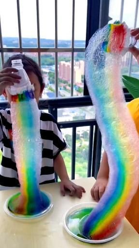 two children sitting at a table covered in fake rainbow colored streamers and drinking water