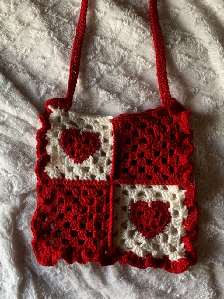 a crocheted red and white purse sitting on top of a bed next to a pillow