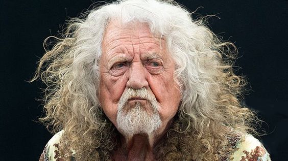 an old man with white hair and long curly hair wearing a floral shirt looking at the camera