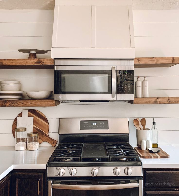 a stove top oven sitting inside of a kitchen next to wooden shelves with dishes on them