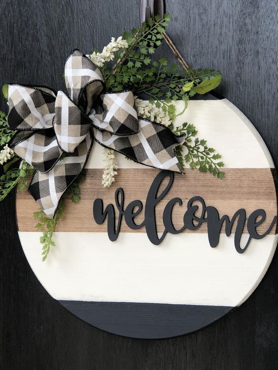 a welcome sign hanging on the side of a door with greenery and ribbon around it