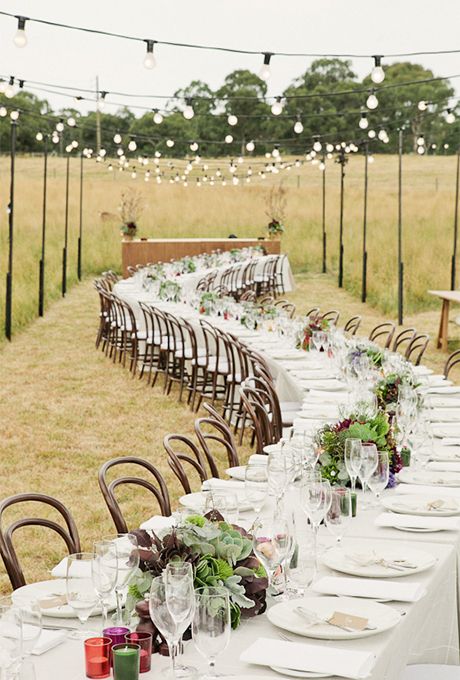 a long table is set up with place settings for an outdoor dinner party in the middle of a field