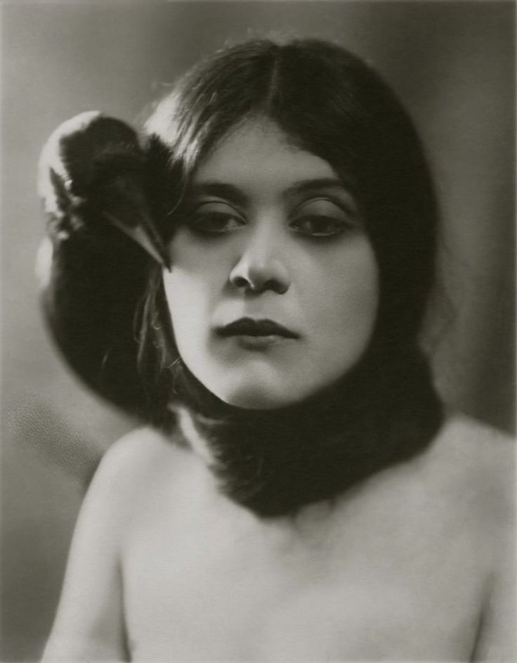 an old black and white photo of a woman with a bird on her shoulder,