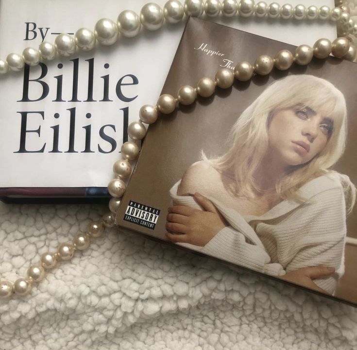 a book and necklace laying on top of a white blanket next to a pair of pearls