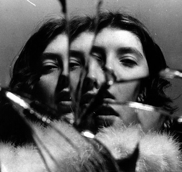 black and white photograph of two women looking at each other's eyes with feathers in front of them