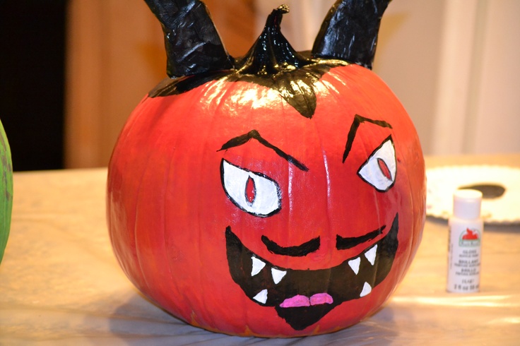 a pumpkin with horns and fangs painted on it's face, sitting on a table