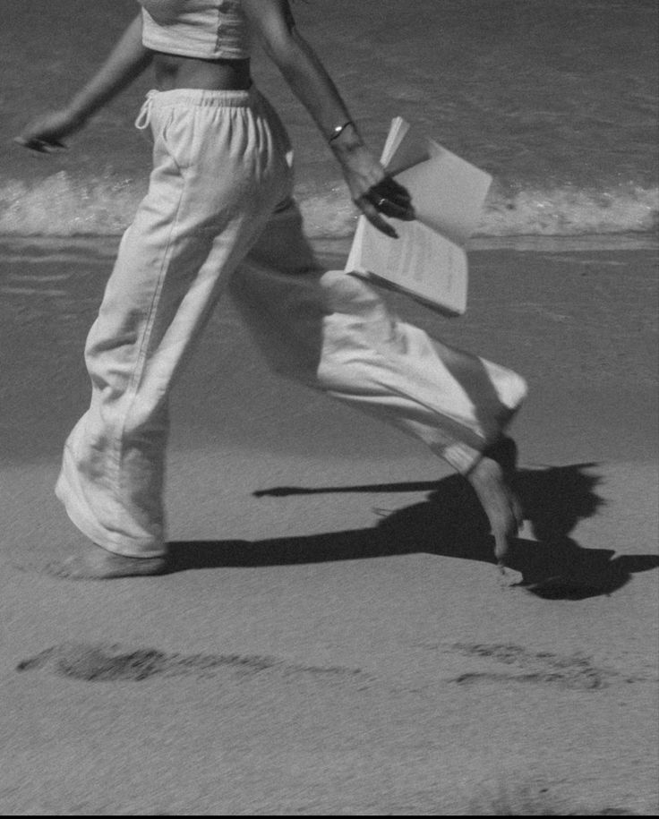 a woman is walking on the beach with books in her hand and writing i love you written in the sand