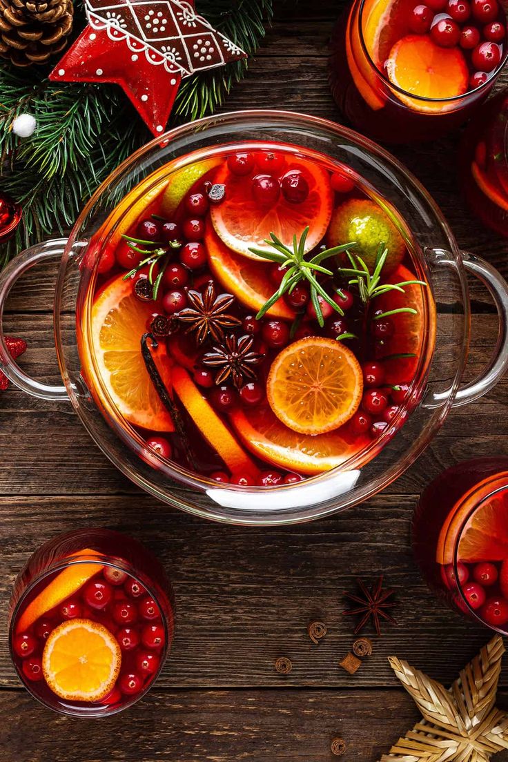 a glass bowl filled with oranges and cranberries next to other christmas decorations