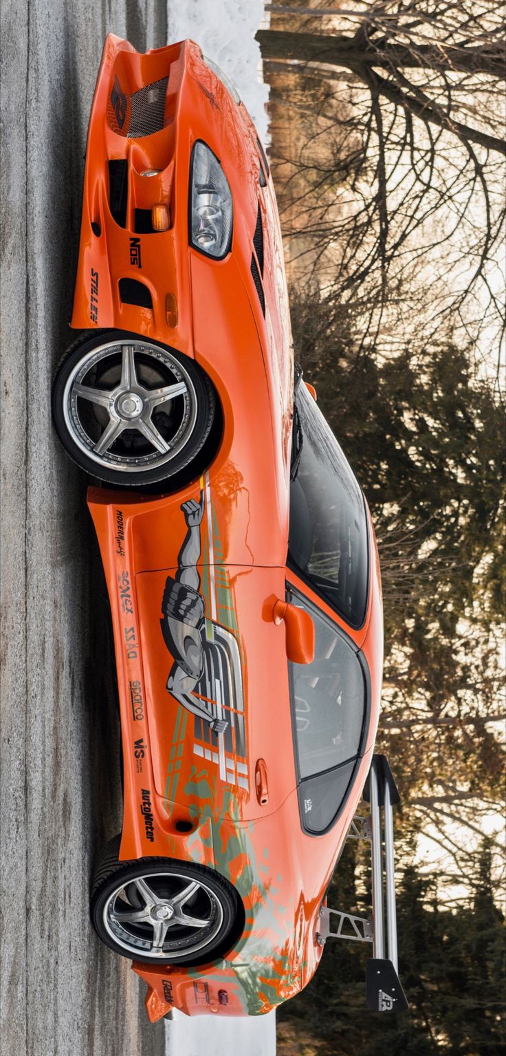 an orange sports car parked on the side of a road next to snow covered trees