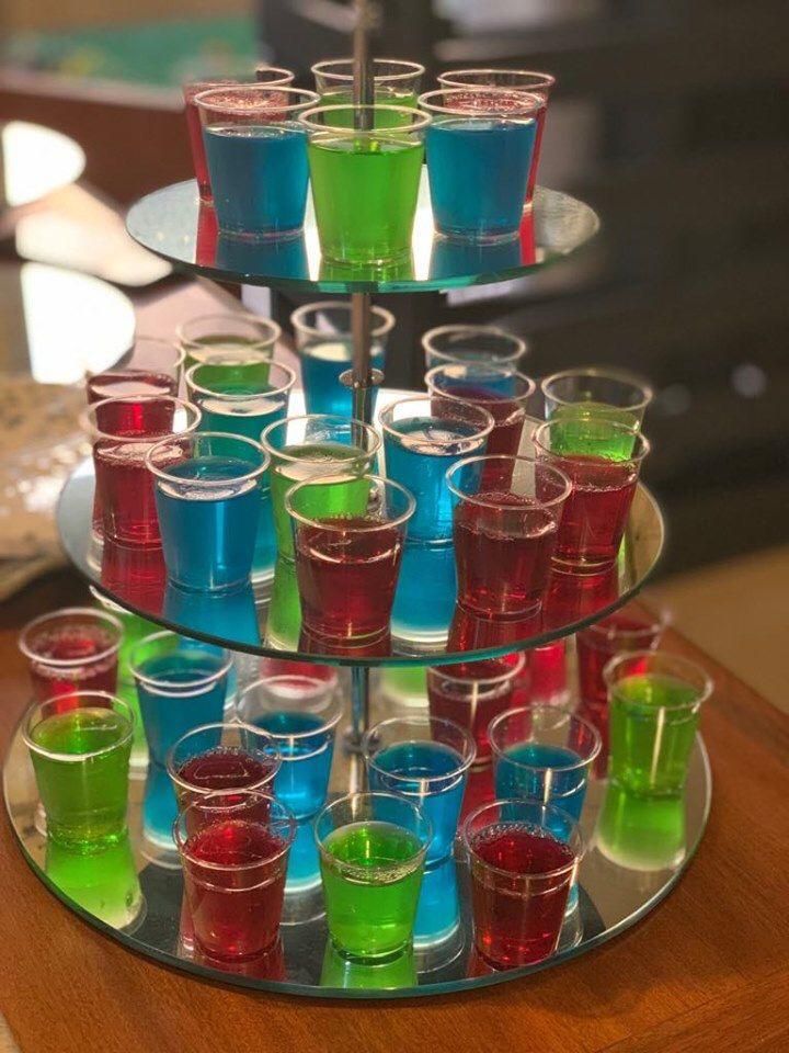 a three tiered tray filled with different colored glasses on top of a wooden table