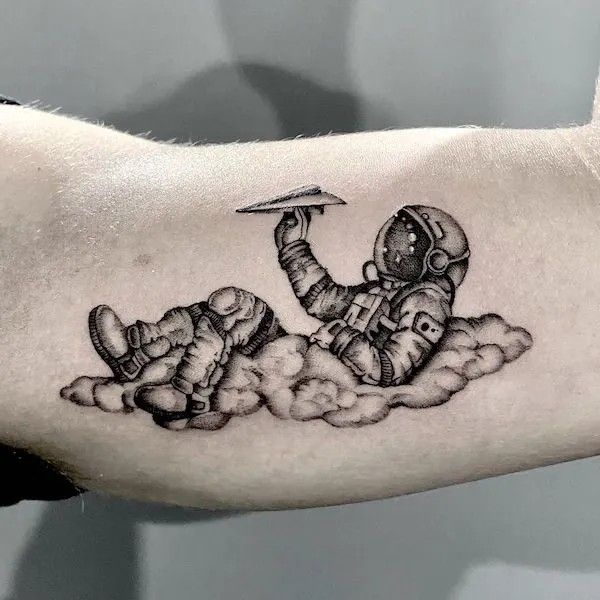 a man's arm with a black and white tattoo of an astronaut in the clouds