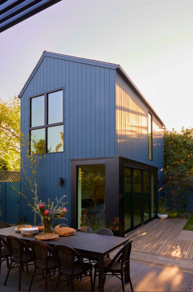 an outdoor dining area with table and chairs next to a blue house in the background