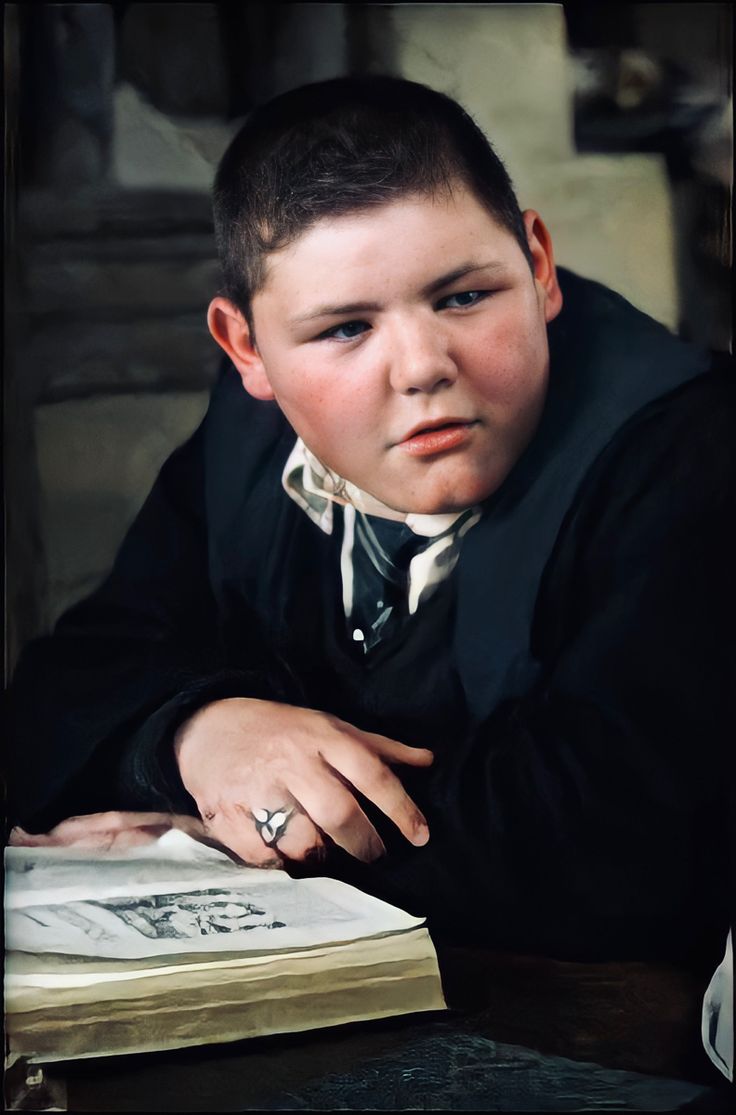 a young boy wearing a suit and tie sitting at a table with an open book