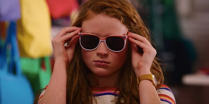 a woman with red hair wearing sunglasses and holding her hands up to her face while looking at the camera