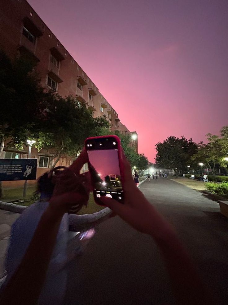 someone holding up their cell phone to take a photo in the street at night time