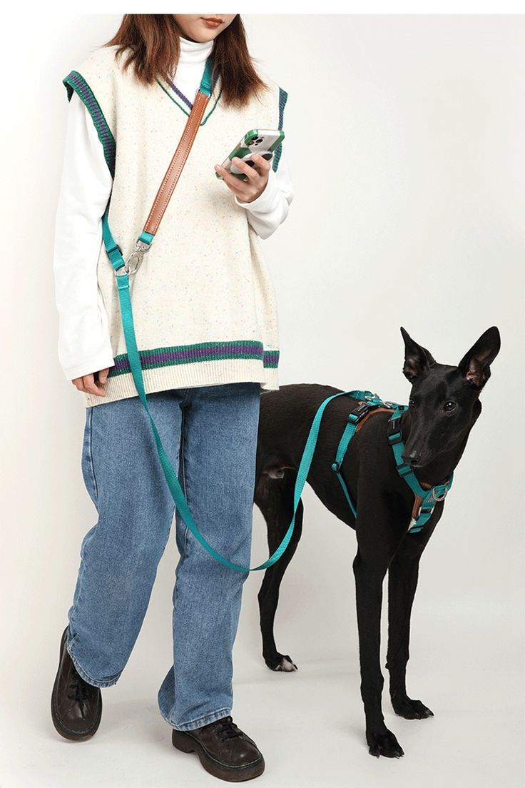 a woman standing next to a black dog wearing a harness and holding a cell phone