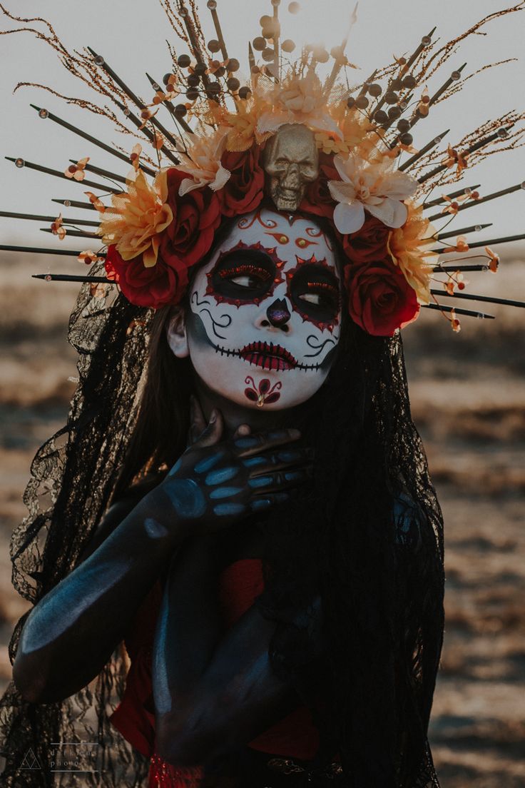 a woman with makeup and flowers on her head is standing in the sand near the ocean