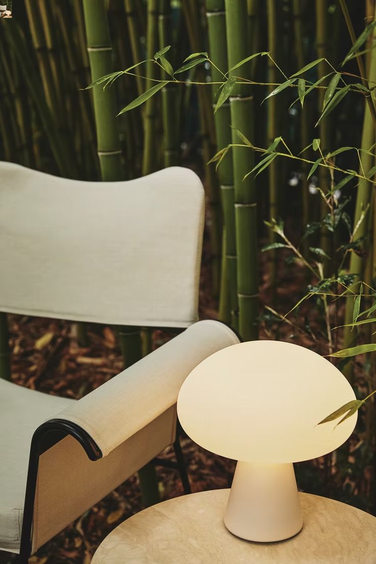 a white table sitting next to a chair in front of a bamboo tree with its lights on