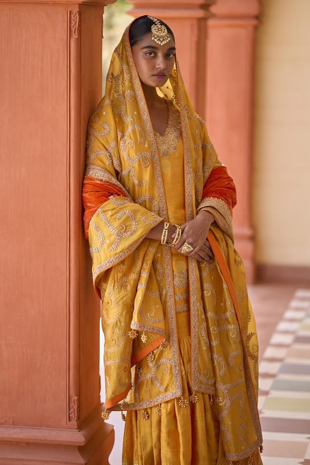 Yellow banarasi silk kurta with all over metallic woven floral, wreath pattern, contrast Mughal jaal pattern, gota, dabka and marodi embroidery. Paired with woven flared gharara and jaal embroidered dupatta.
Components: 3
Pattern: Woven and Embroidered
Type Of Work: Floral Pattern, Dabka, Gota and Marodi Work
Neckline: V Neck
Sleeve Type: Three Quarter Sleeves
Fabric: Banarasi Silk, Organza Silk
Color: Yellow
Other Details: 
Scalloped cut work neckline
Drop tasselled dupatta border
Note:
The ora Traditional Sharara With Gota Work And Straight Kurta, Traditional Sharara With Gota Work, Traditional Sharara With Gota Work For Eid, Festive Kundan Sharara With Cutdana Details, Sharara With Gota Work For Eid, Unstitched Bollywood Sharara With Cutdana, Semi-stitched Chandbali Sharara For Transitional Season, Floor-length Chanderi Sharara With Dupatta, Yellow Semi-stitched Sharara For Transitional Season