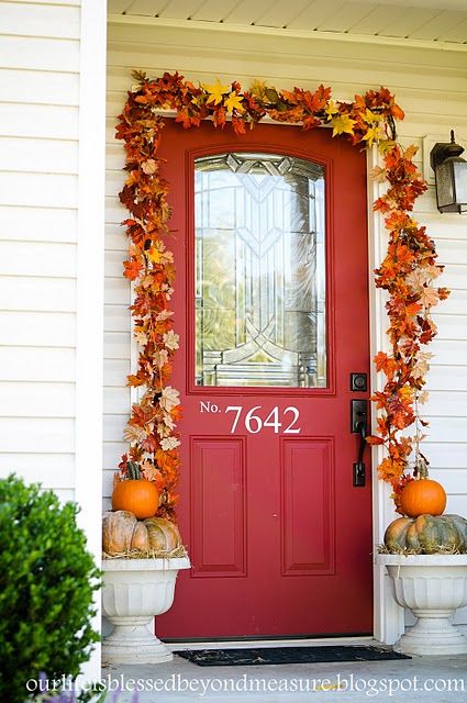 a red front door decorated with fall leaves and pumpkins